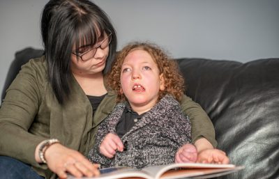 A loving mother reads a book to her daughter who has cerebral palsy.